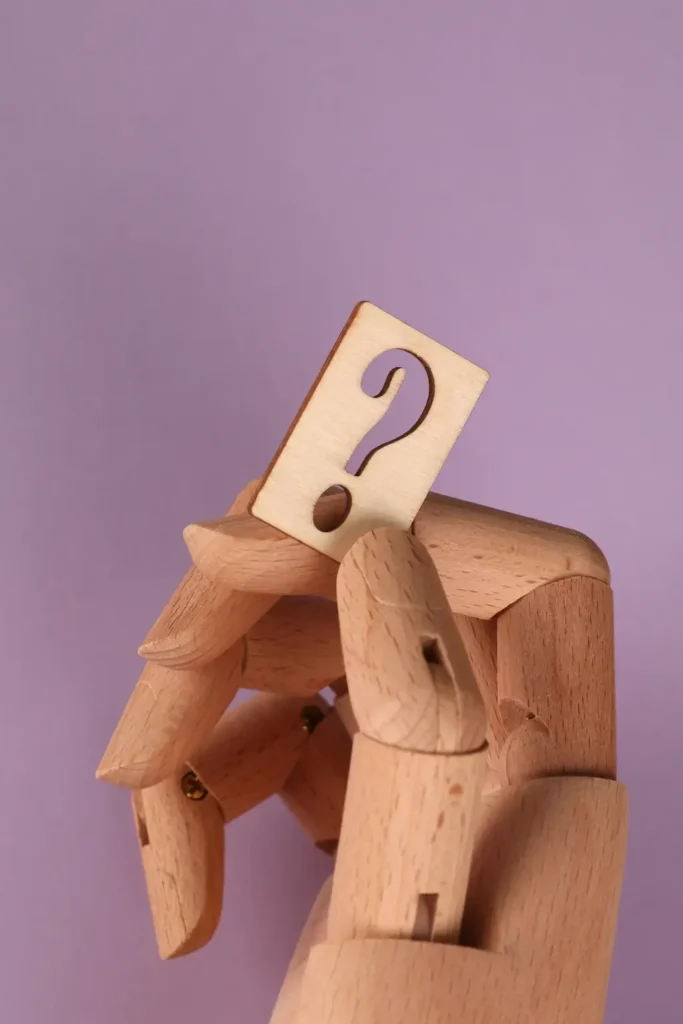 A wooden robot stands holding a wooden question mark, symbolizing curiosity and inquiry in a playful design.